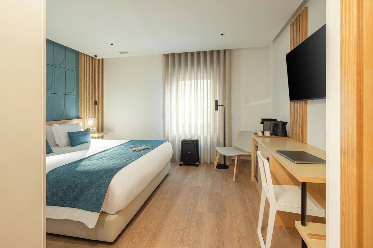 A hotel room with a bed, desk, chair, television, and curtains.