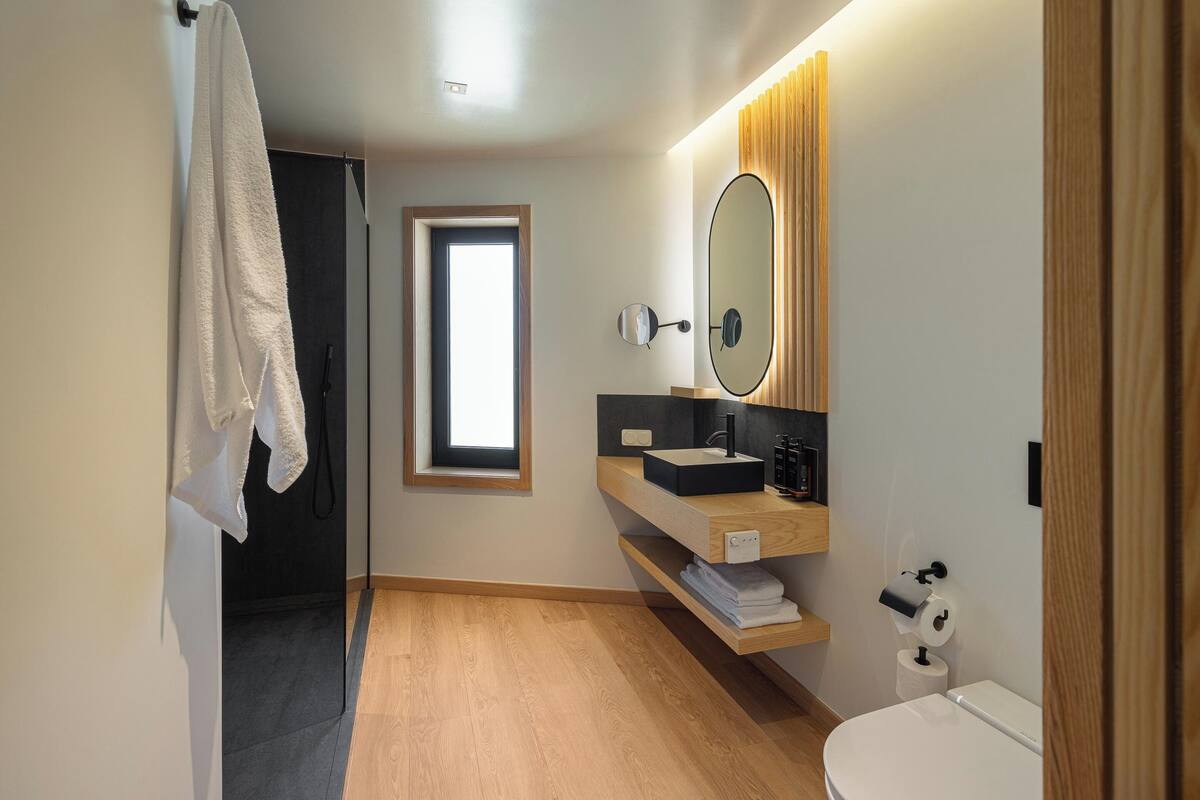 A modern bathroom with a wooden floor, a white sink, a mirror, and a toilet.