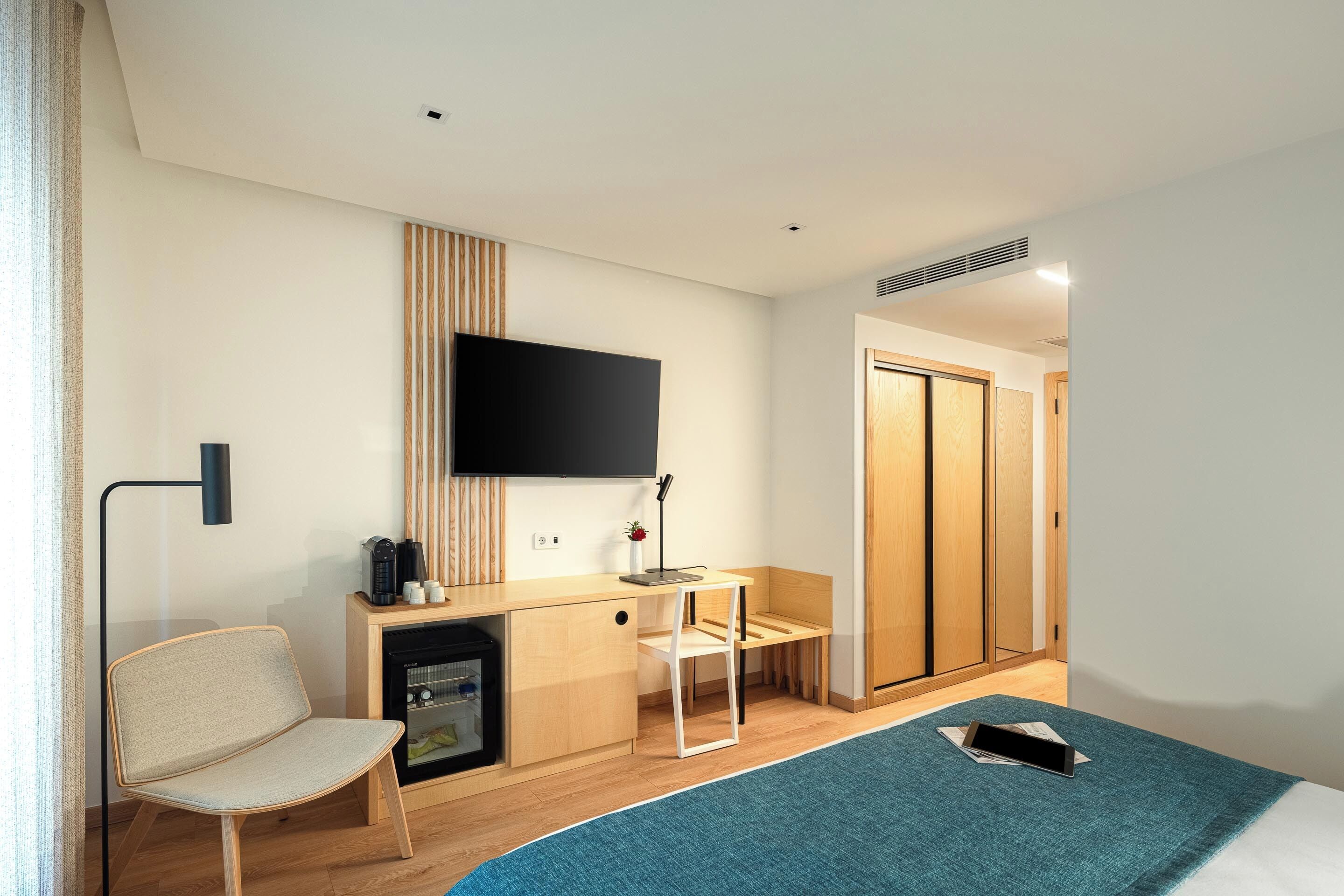 Una habitación de hotel moderna con cama, escritorio, silla, televisor y armario.