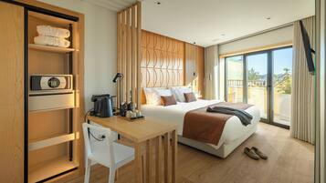 A modern hotel room with a bed, a desk with a chair, a coffee maker, and a view through large windows.