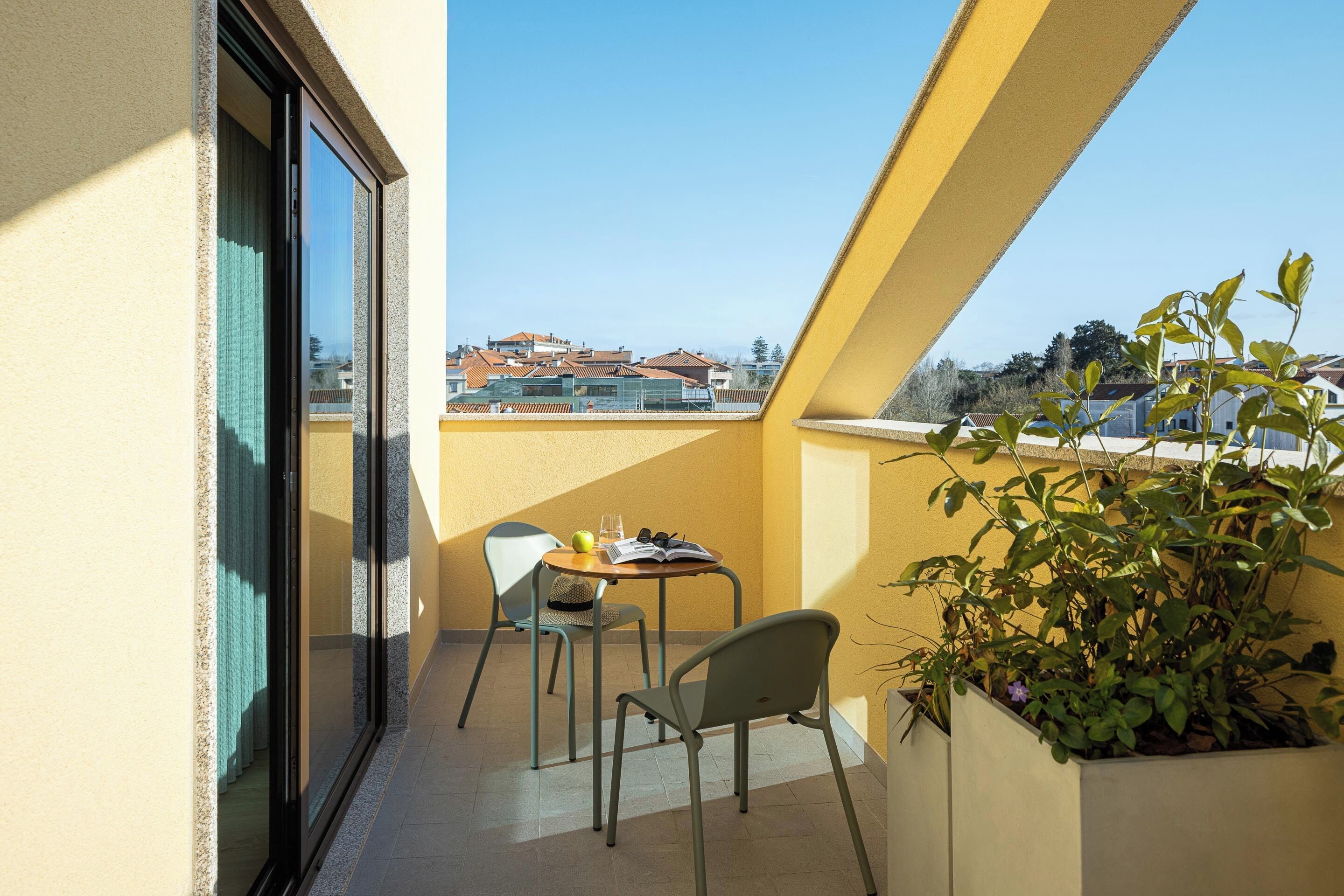 Un balcón con una mesa, sillas, una planta y vistas a edificios.