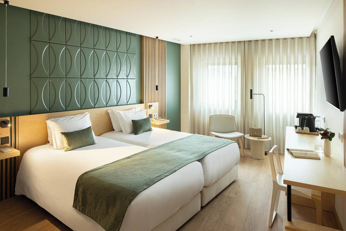 A hotel room with a large bed, a desk, a chair, a TV, and a window with curtains.