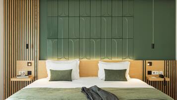 Habitación de hotel moderna con una cama grande, dos mesitas de noche, cabecera con iluminación integrada y una pared de acento verde.