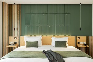 Habitación de hotel moderna con una cama grande, dos mesitas de noche, cabecera con iluminación integrada y una pared de acento verde.