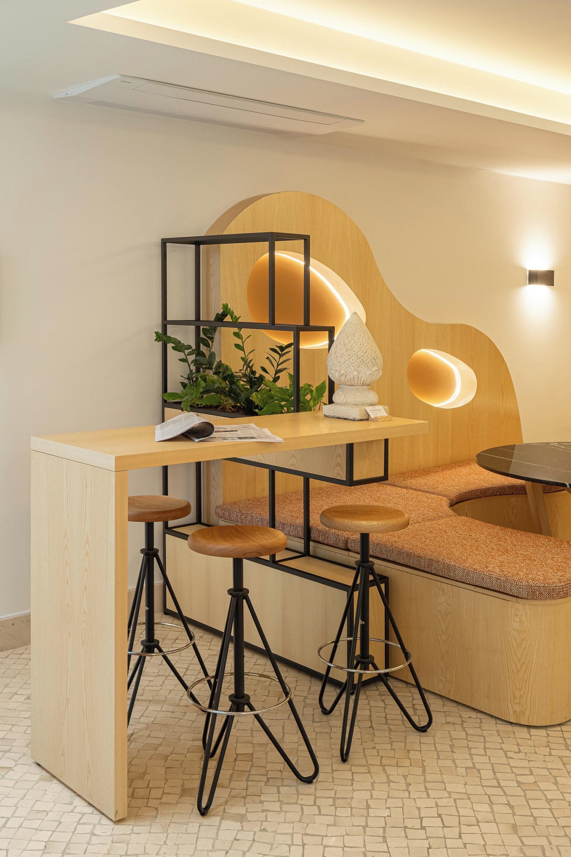 Un área de bar moderna con mostrador de madera, taburetes y una planta decorativa.