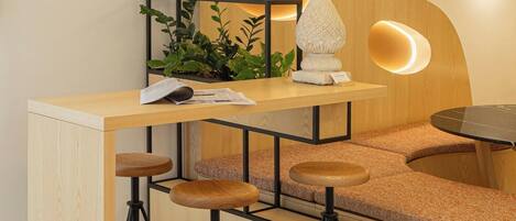 Un área de bar moderna con mostrador de madera, taburetes y una planta decorativa.
