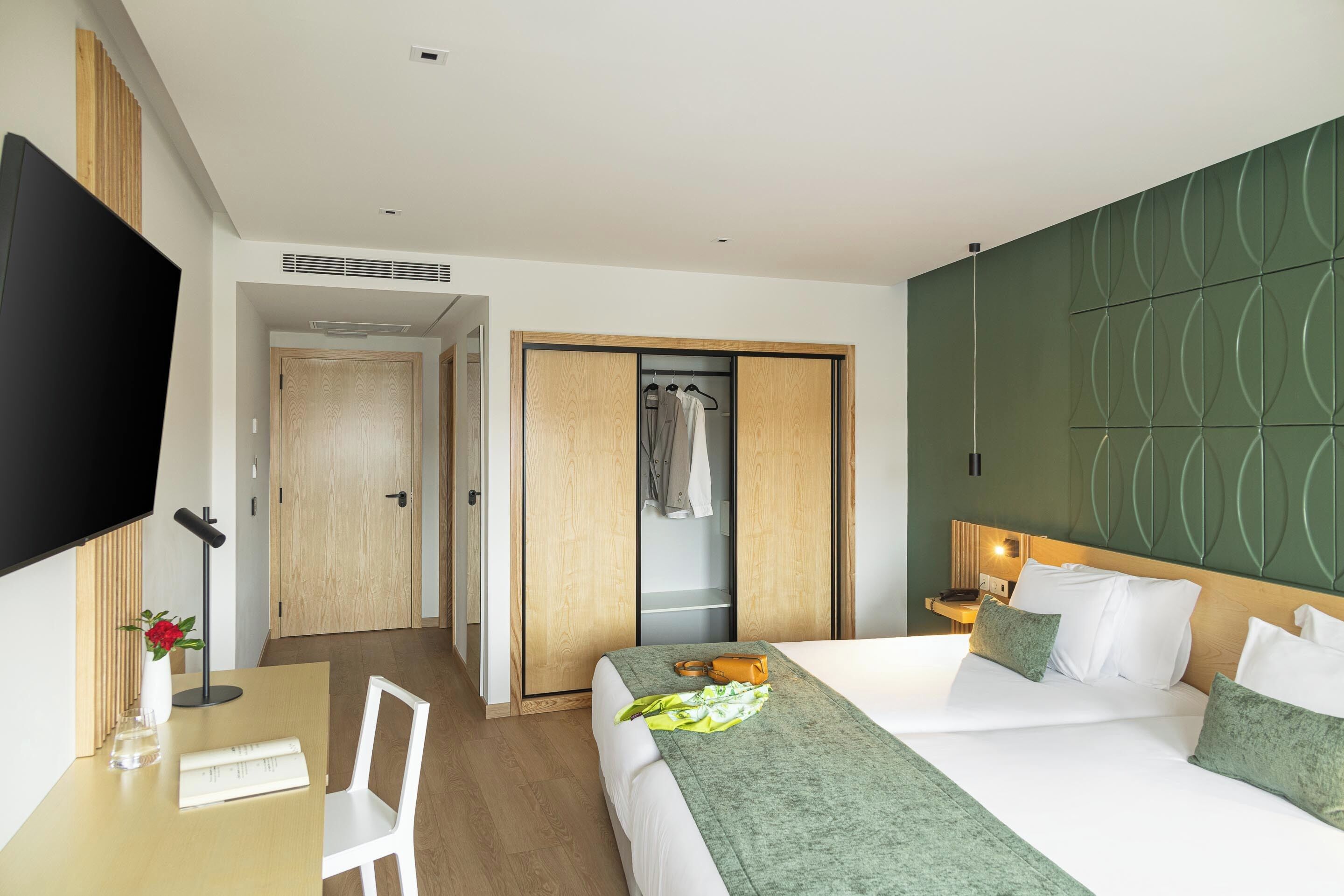 Quarto de hotel com uma cama, uma escrivaninha com cadeira, uma televisão e um guarda-roupa.