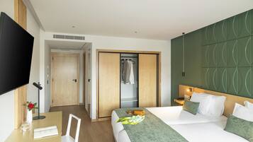 Quarto de hotel com uma cama, uma escrivaninha com cadeira, uma televisão e um guarda-roupa.
