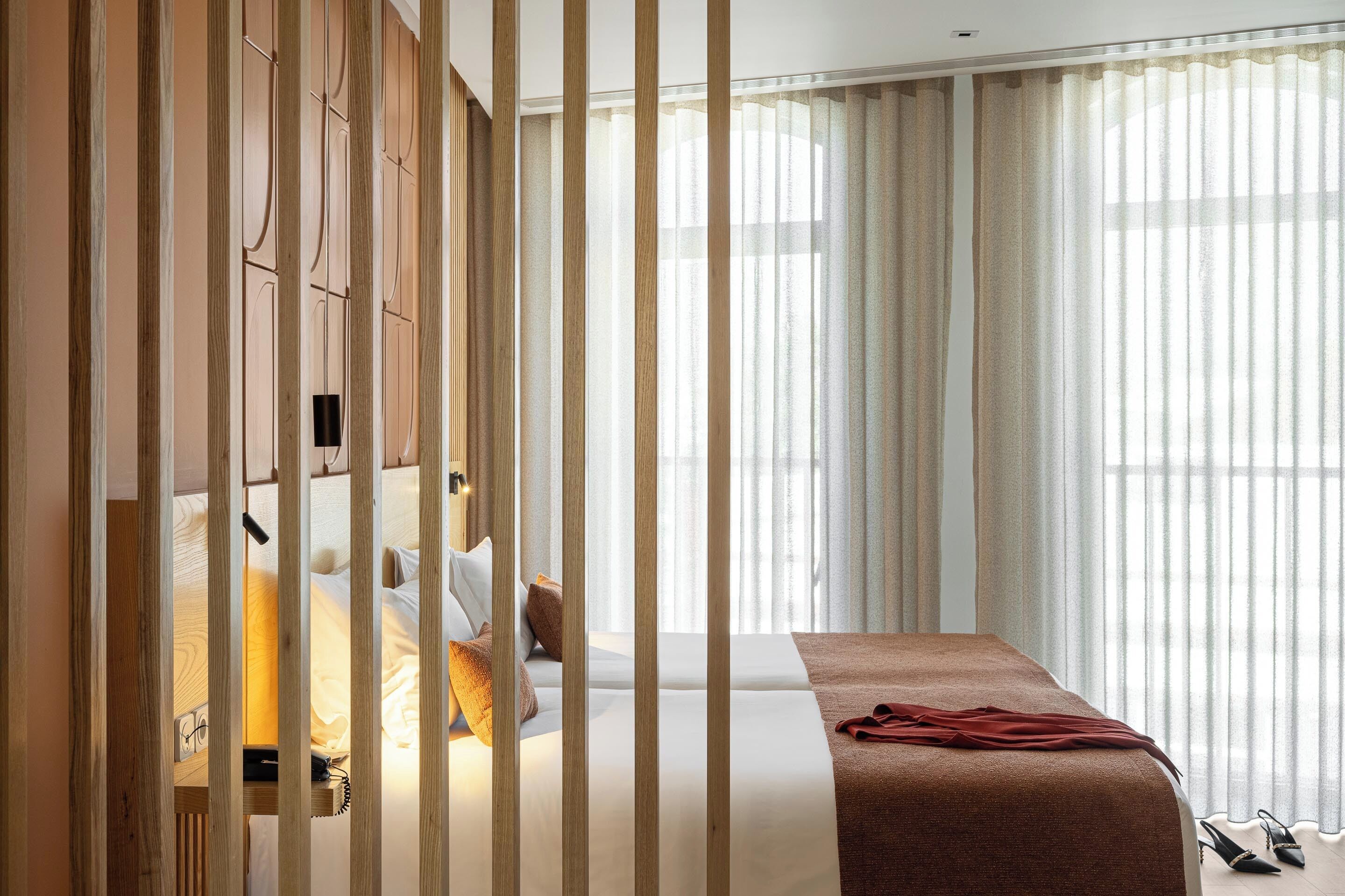 A hotel room with a bed, a wooden partition, and sheer curtains.