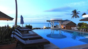Ein Poolbereich mit Liegestühlen, einer Laube und Blick aufs Meer.