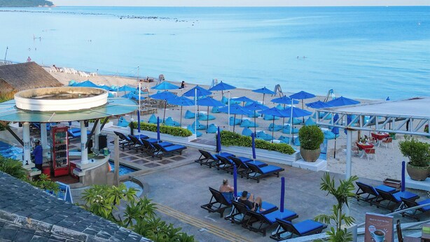 Ein Strandresort mit Liegestühlen und Sonnenschirmen, einem Poolbereich und Blick aufs Meer.