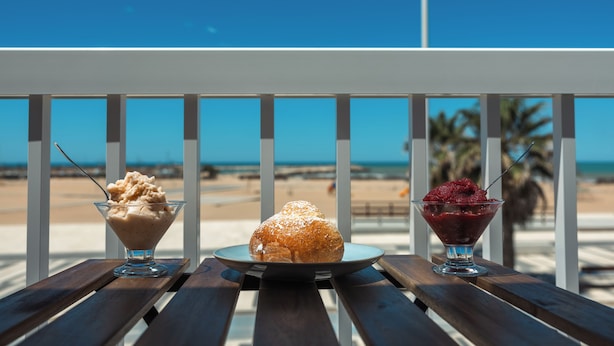Une table de desserts avec trois plats, disposés sur un banc en bois donnant sur une plage.