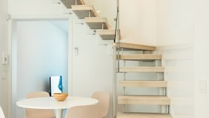 Un intérieur moderne avec un escalier en colimaçon, une table de salle à manger ronde entourée de chaises et un design minimaliste.