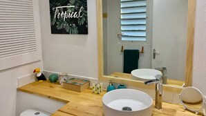 A bathroom with a wooden vanity, a white sink, a large mirror, and a framed picture on the wall. - Charming studio in the very pleasant district of Orient Bay (SAINT MARTIN)