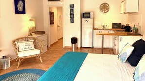 A compact bedroom with a bed, a chair, a desk, and a kitchenette. - Charming studio in the very pleasant district of Orient Bay (SAINT MARTIN)