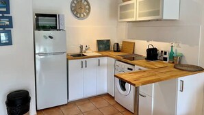 A compact kitchen with white cabinets, a microwave, a refrigerator, a washing machine, and a wooden countertop. - Charming studio in the very pleasant district of Orient Bay (SAINT MARTIN)