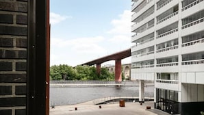 A view of a parking area with a bridge in the background, a body of water, and a modern building with multiple floors. - Stylish Luxe home by the water (Stockholms län)