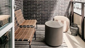 A modern balcony with a brick wall, a wicker sofa, a round table, and a patterned rug. - Stylish Luxe home by the water (Stockholms län)