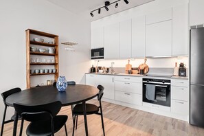 Una cocina moderna con gabinetes blancos, encimera negra, mesa de comedor de madera con sillas y horno empotrado.
