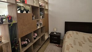 A bedroom with a wooden wardrobe, a bedside table with a lamp, and a floral-patterned bedspread.