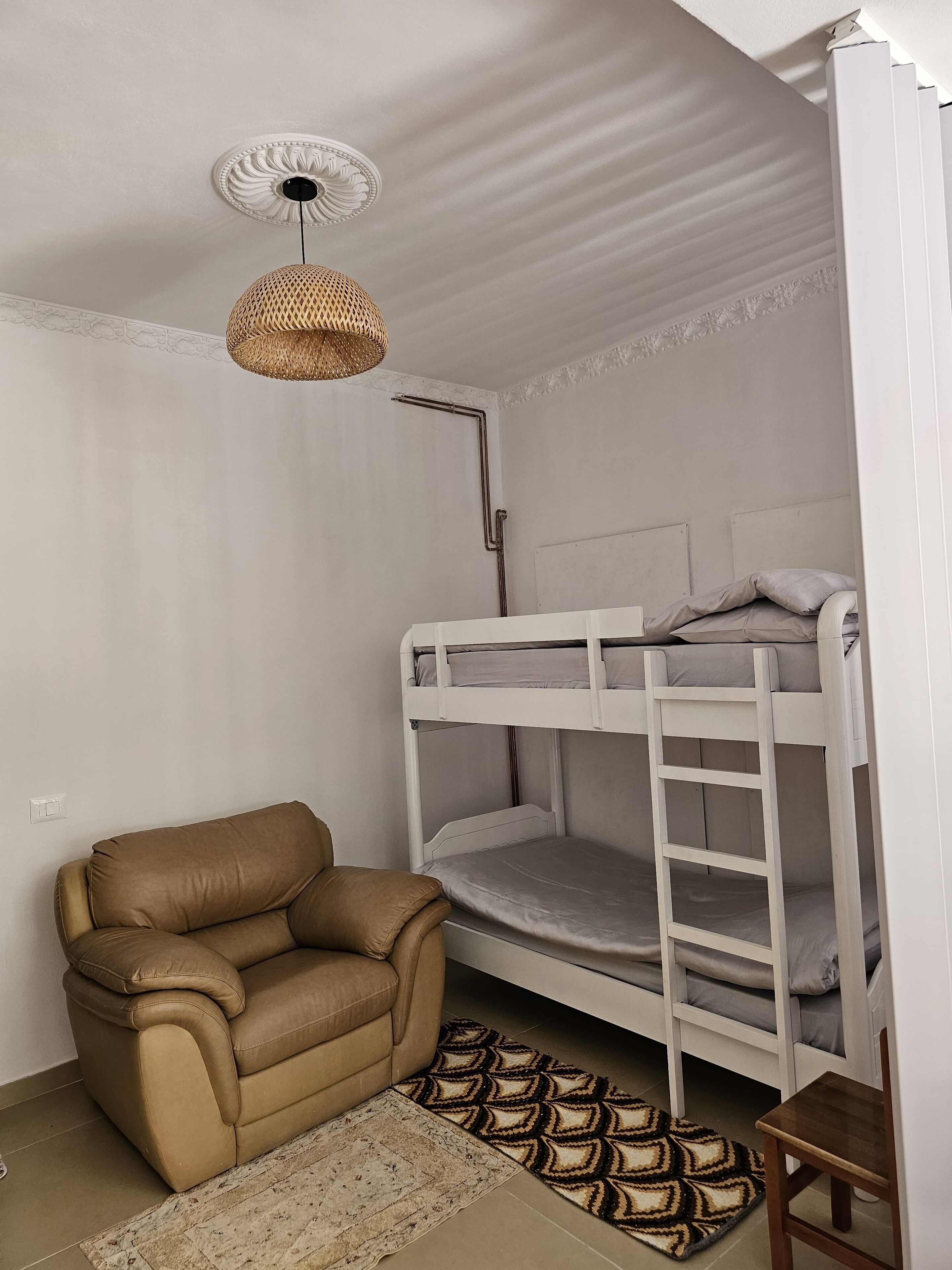 A bunk bed with a ladder, a brown leather chair, a woven floor lamp, and a patterned rug.