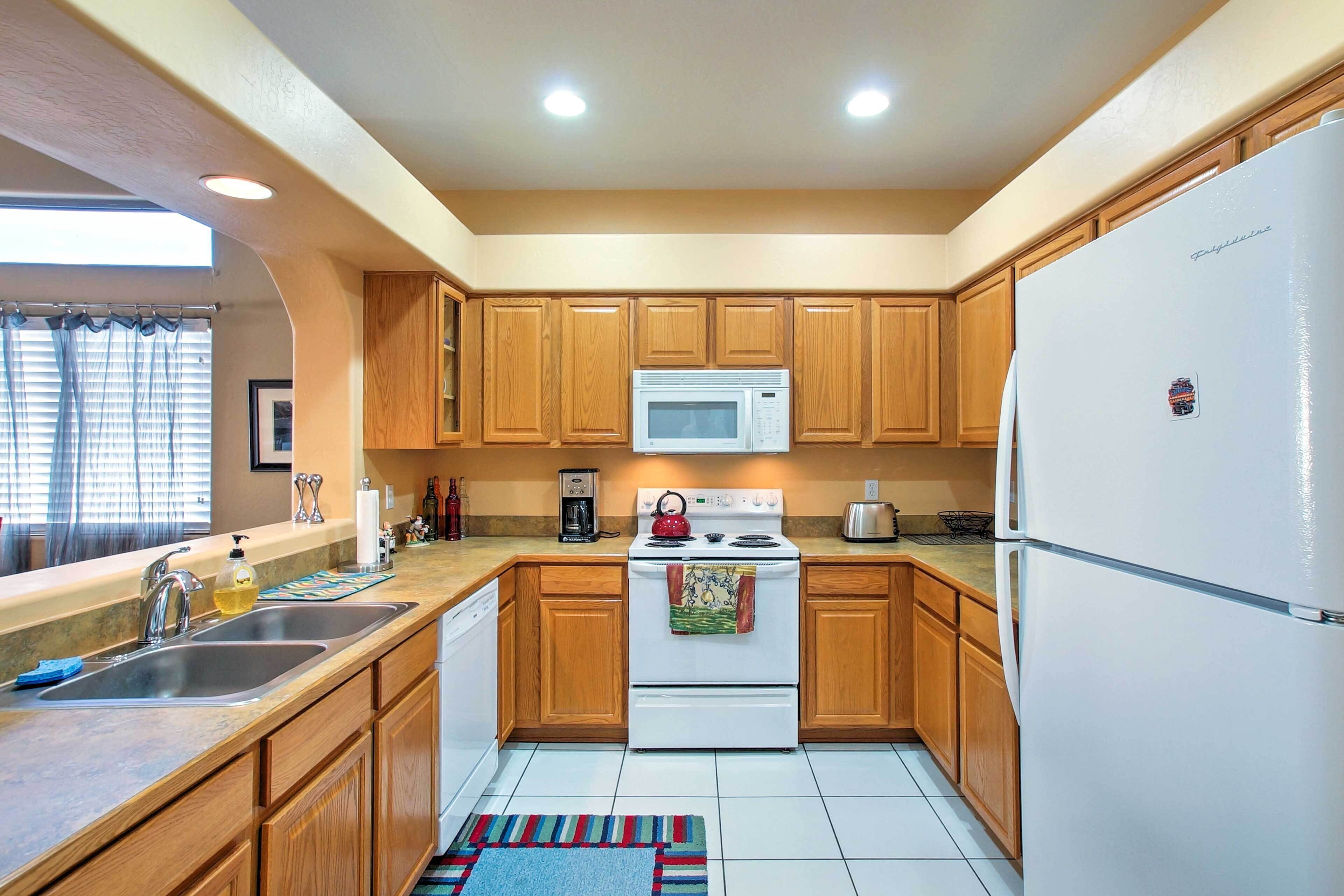 A compact kitchen with wooden cabinets, a white refrigerator, a microwave, a stove, and a sink.