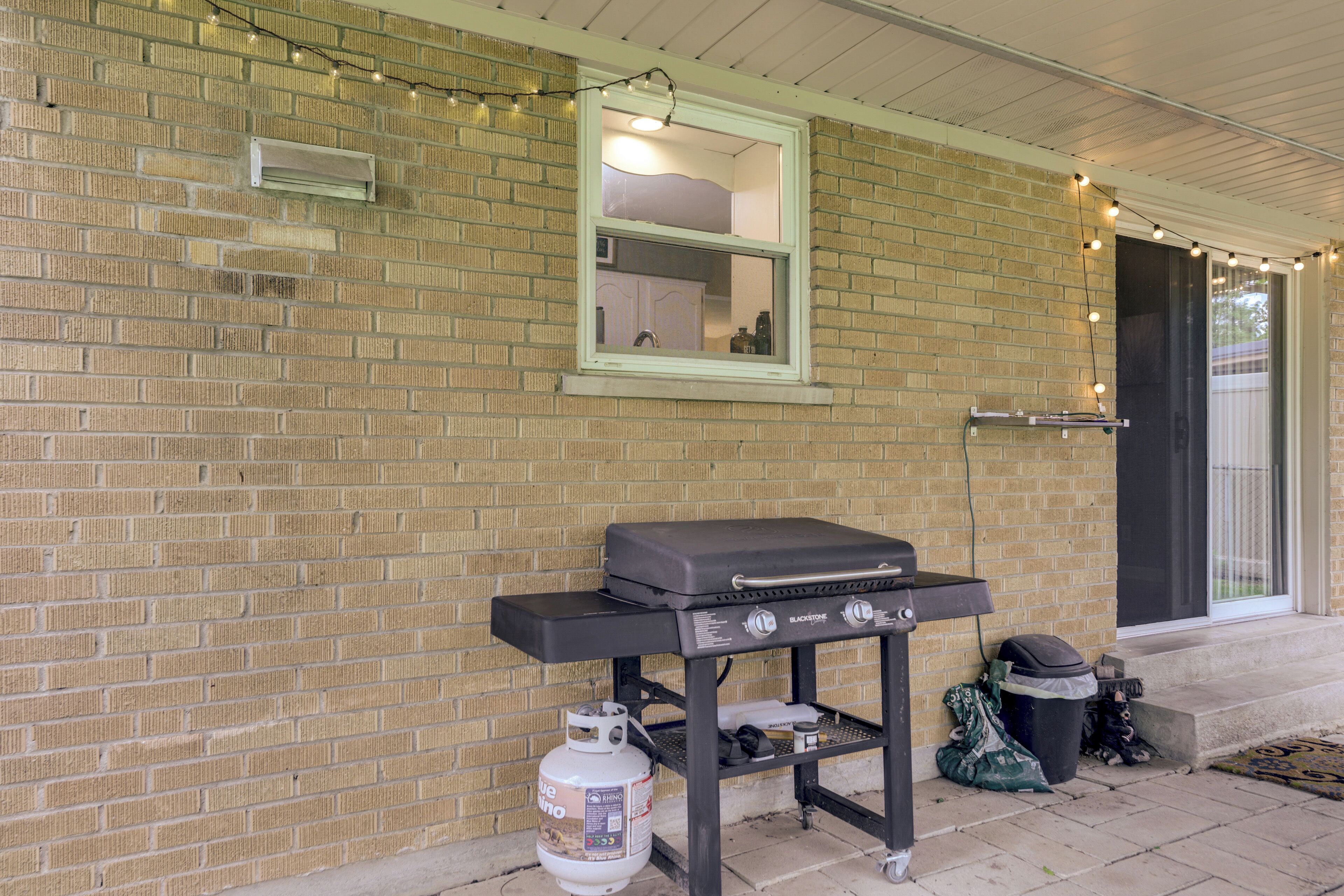 A brick exterior wall with a window, a grill on a cart, and a propane tank.