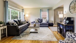 A modern living room with a sofa, coffee table, and a cabinet with a clock. - 10 Mi to Dtwn Cincinnati: Home w/ Patio & Yard! (Cincinnati)