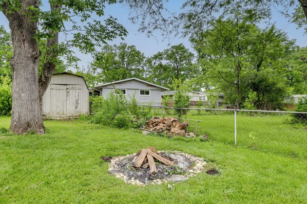 A backyard with a wooden shed, a pile of firewood, and a tree.