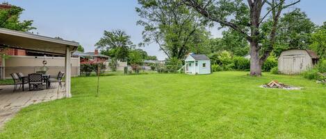 A backyard with a patio, a small shed, and a large tree.