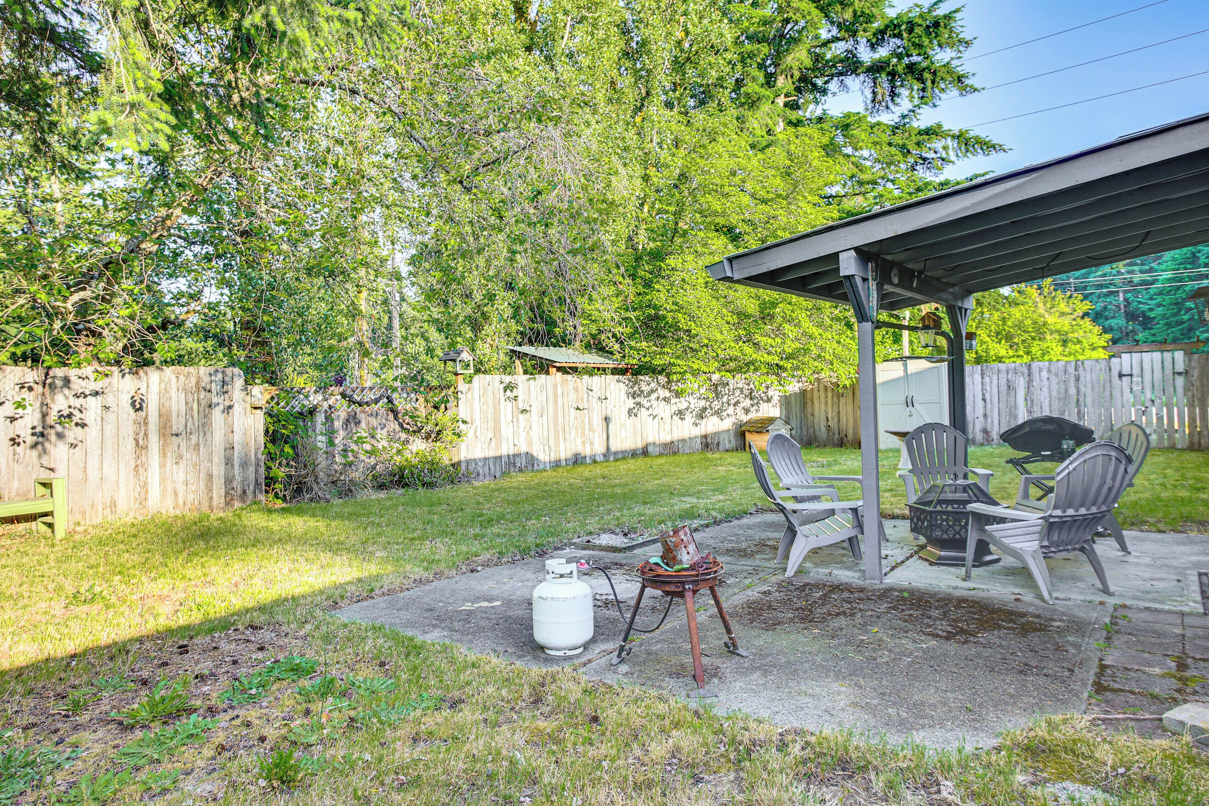 A backyard with a covered patio, outdoor seating, and a propane tank.