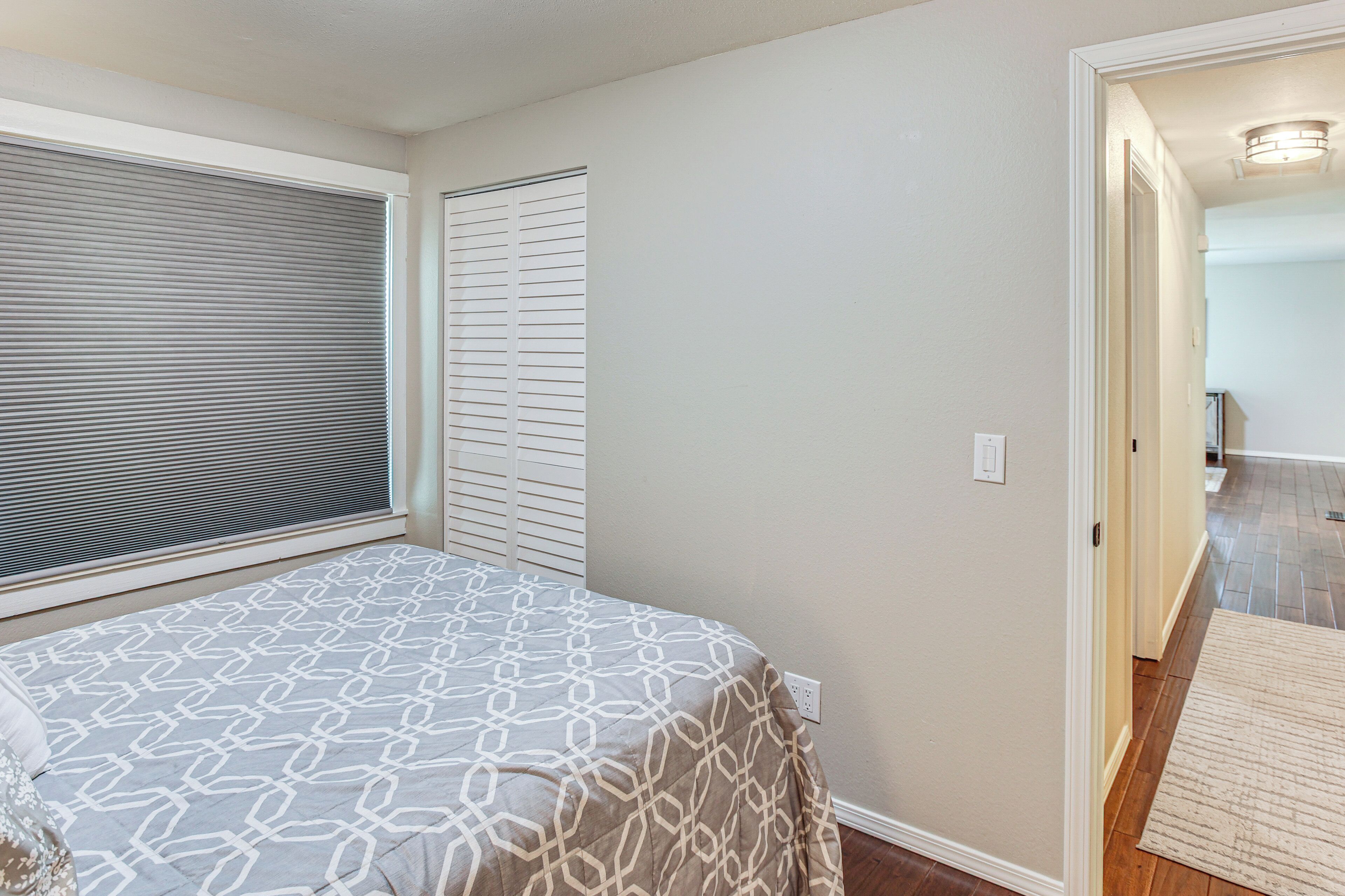 A bedroom with a bed, a window with blinds, a closet, and a hallway leading to another room.