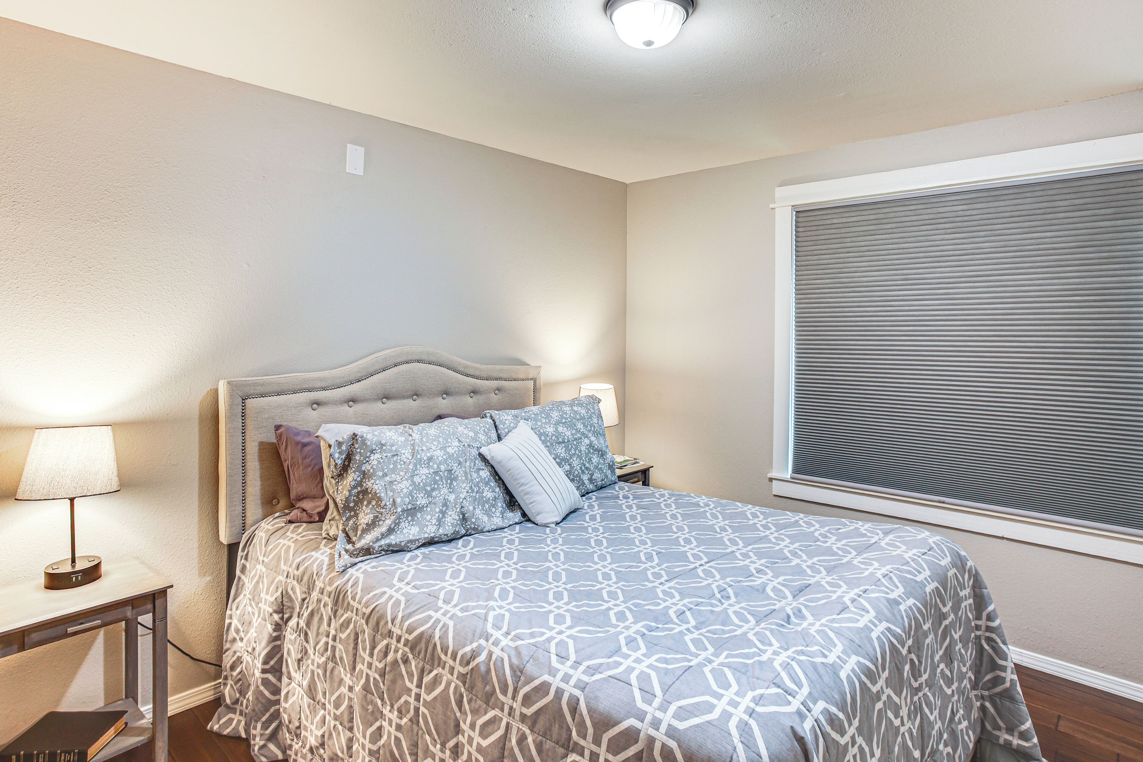 A bedroom with a bed, nightstand, lamp, and window with blinds.