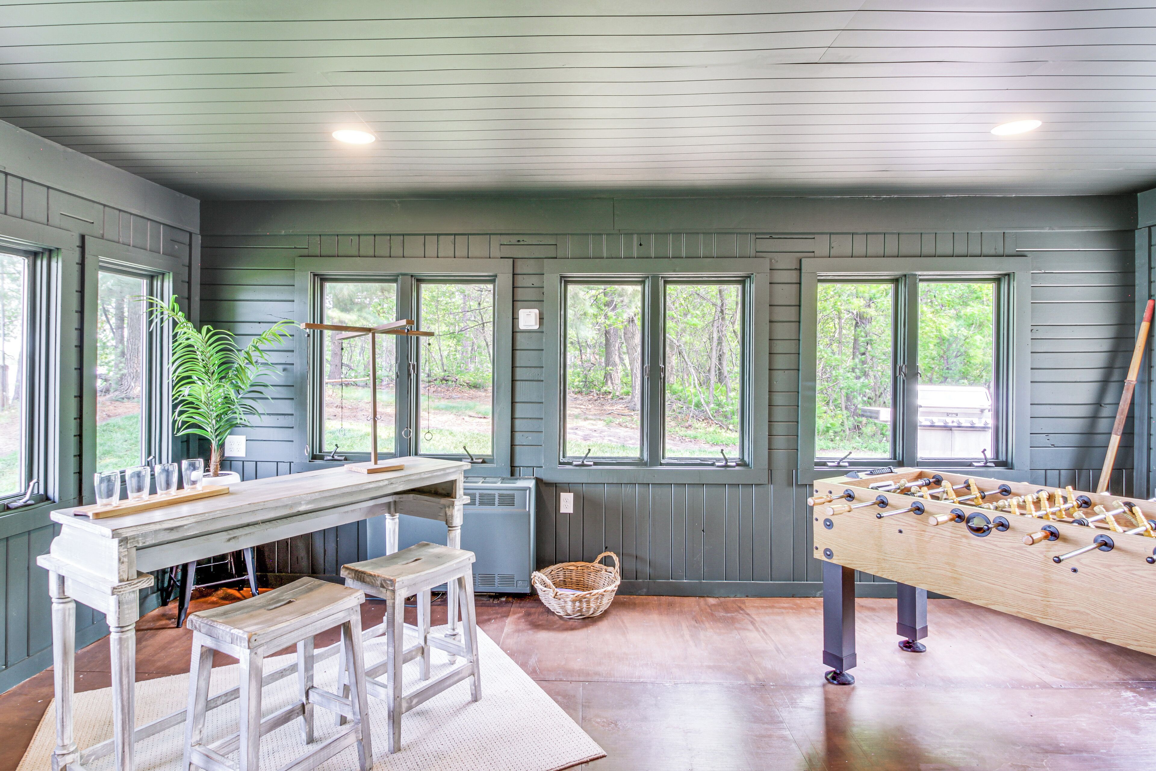 A room with a pool table, bar area, and large windows offering views of the outdoors.