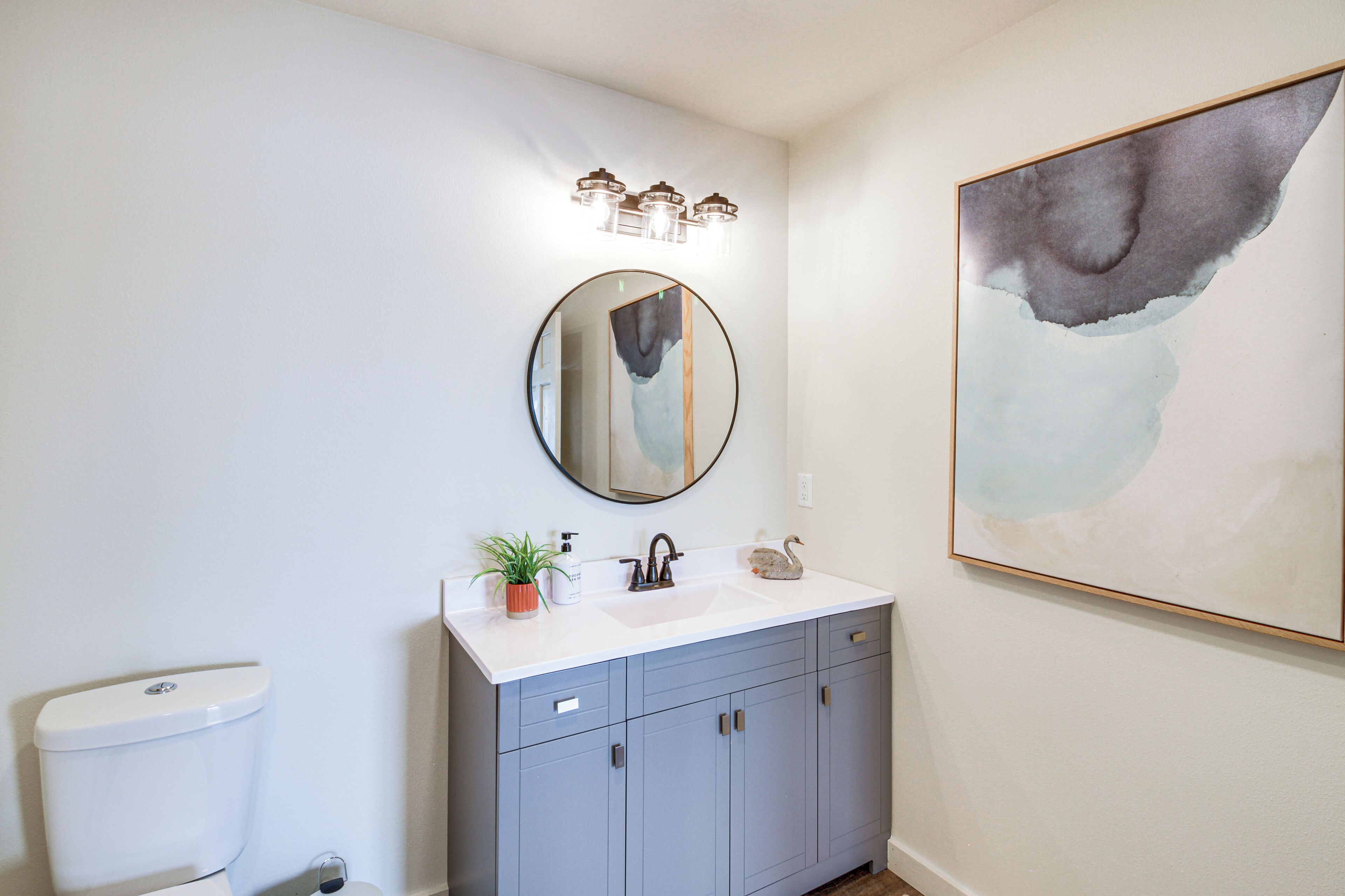 A bathroom with a white sink, a round mirror, and a light fixture above it.