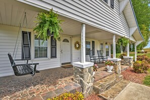 A porch with a swing chair, a potted plant, and a stone column. - Dobson Farmhouse w/ Wraparound Porch & Fire Pit! (Elkin)