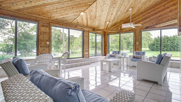 Un vaste espace intérieur doté d’un plafond en bois et de grandes fenêtres offrant une vue sur la verdure.