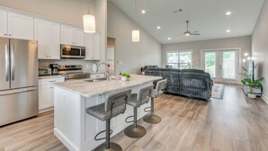 A modern kitchen with white cabinetry, stainless steel appliances, and a central island with bar stools. - Modern Family Home w/ Spacious Yard in Milton (Milton)