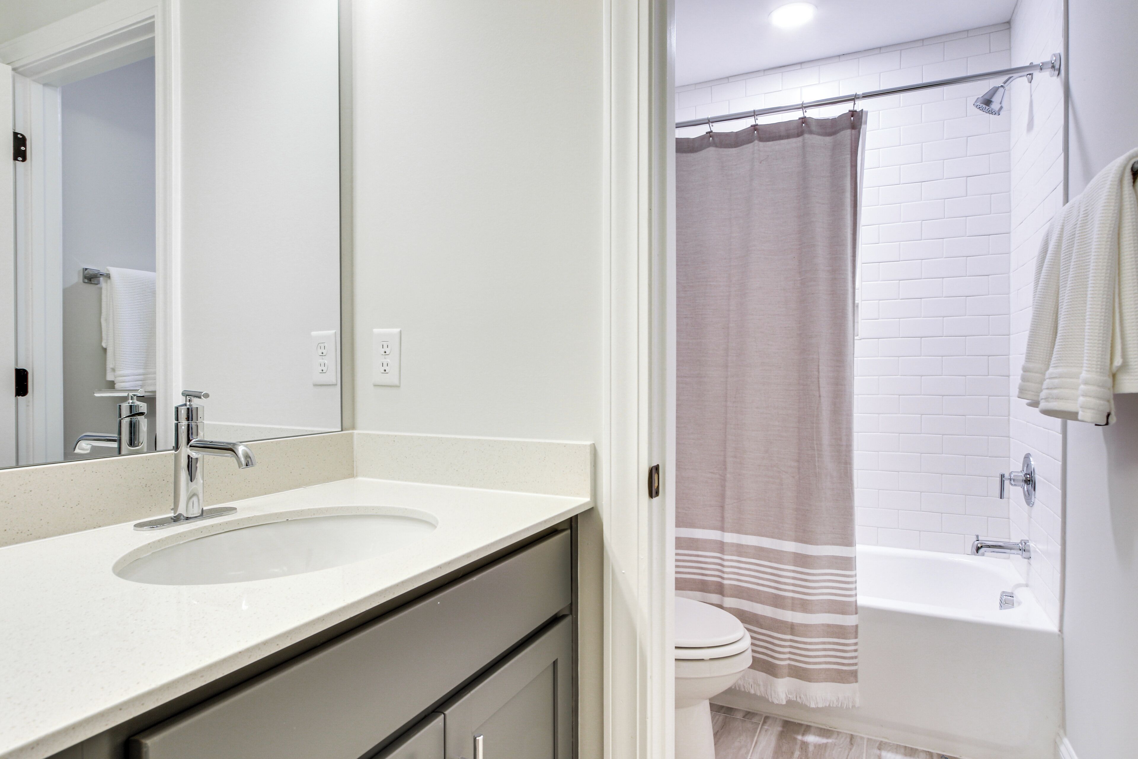 Une salle de bain moderne avec un lavabo blanc, un miroir et un espace douche agrémenté d’un rideau beige.