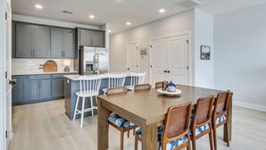 Une cuisine moderne avec des meubles gris, un îlot en bois, des chaises blanches et une table à manger avec des chaises en osier.
