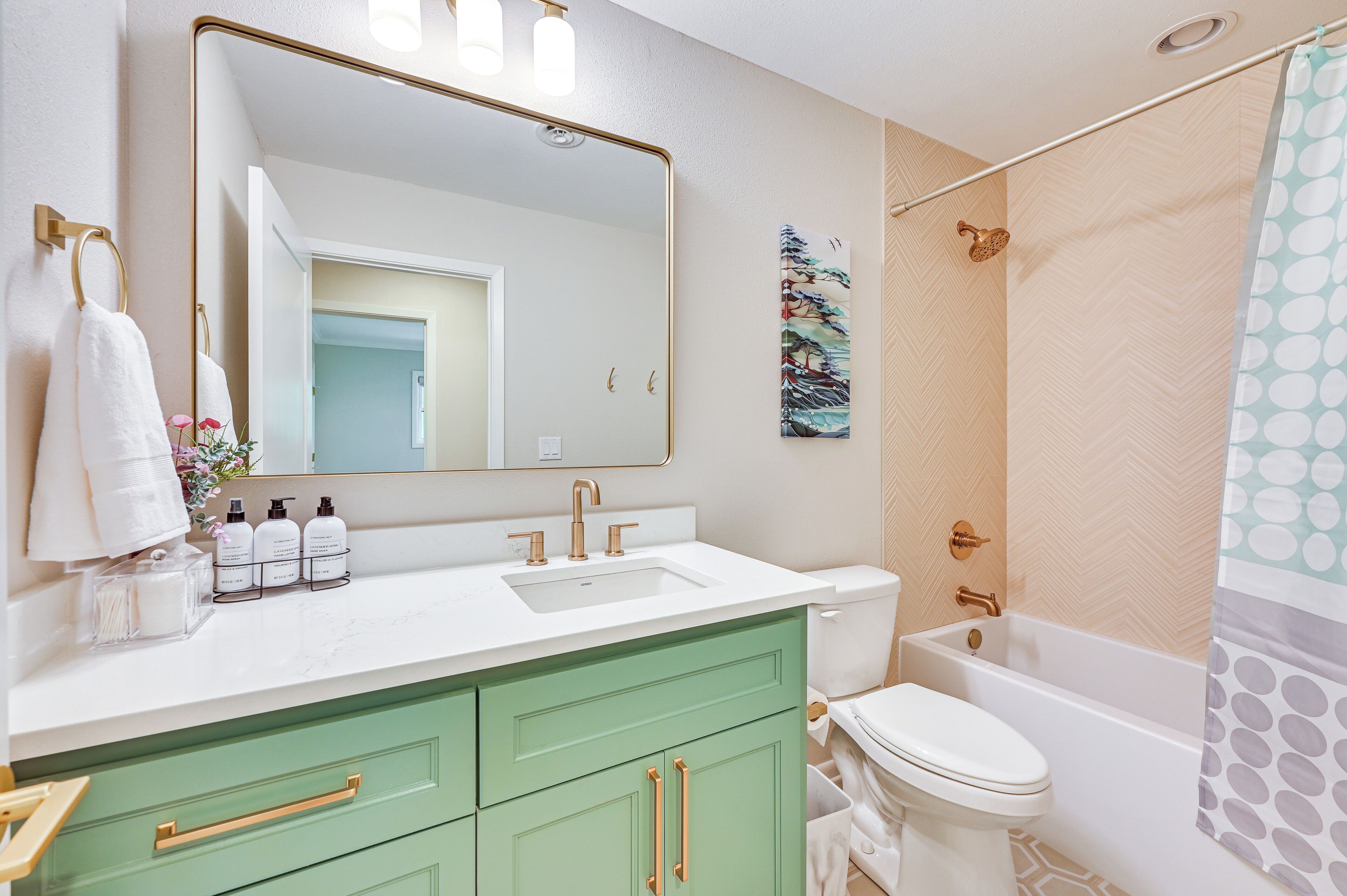 Een badkamer met een witte wastafel, groene kastjes, een wit toilet en een douchegordijn met stippen.