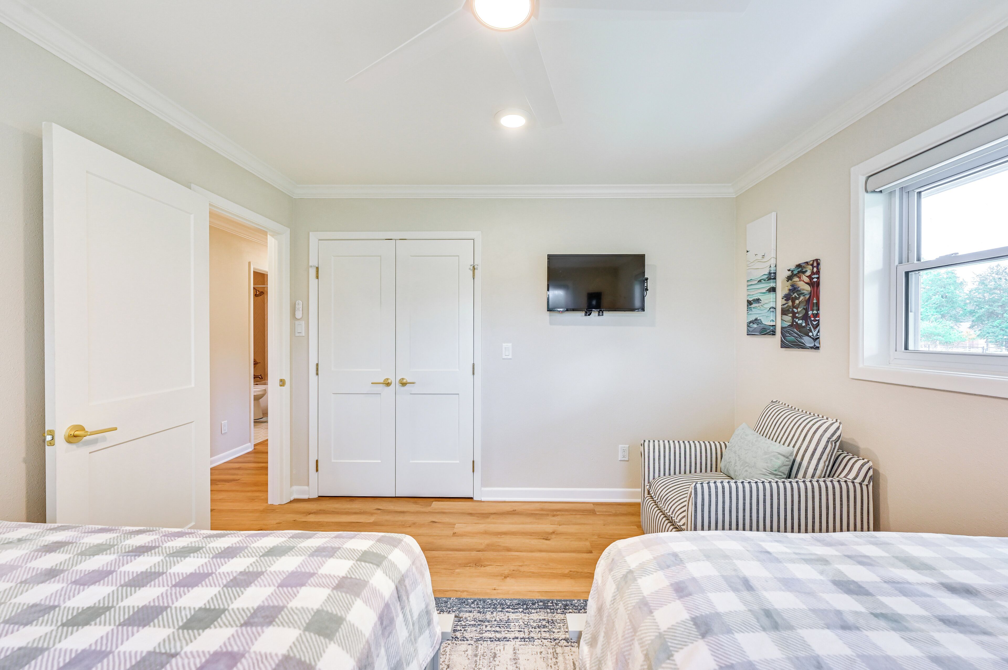 A bedroom with two beds, a window, a door, and a mirror on the wall.