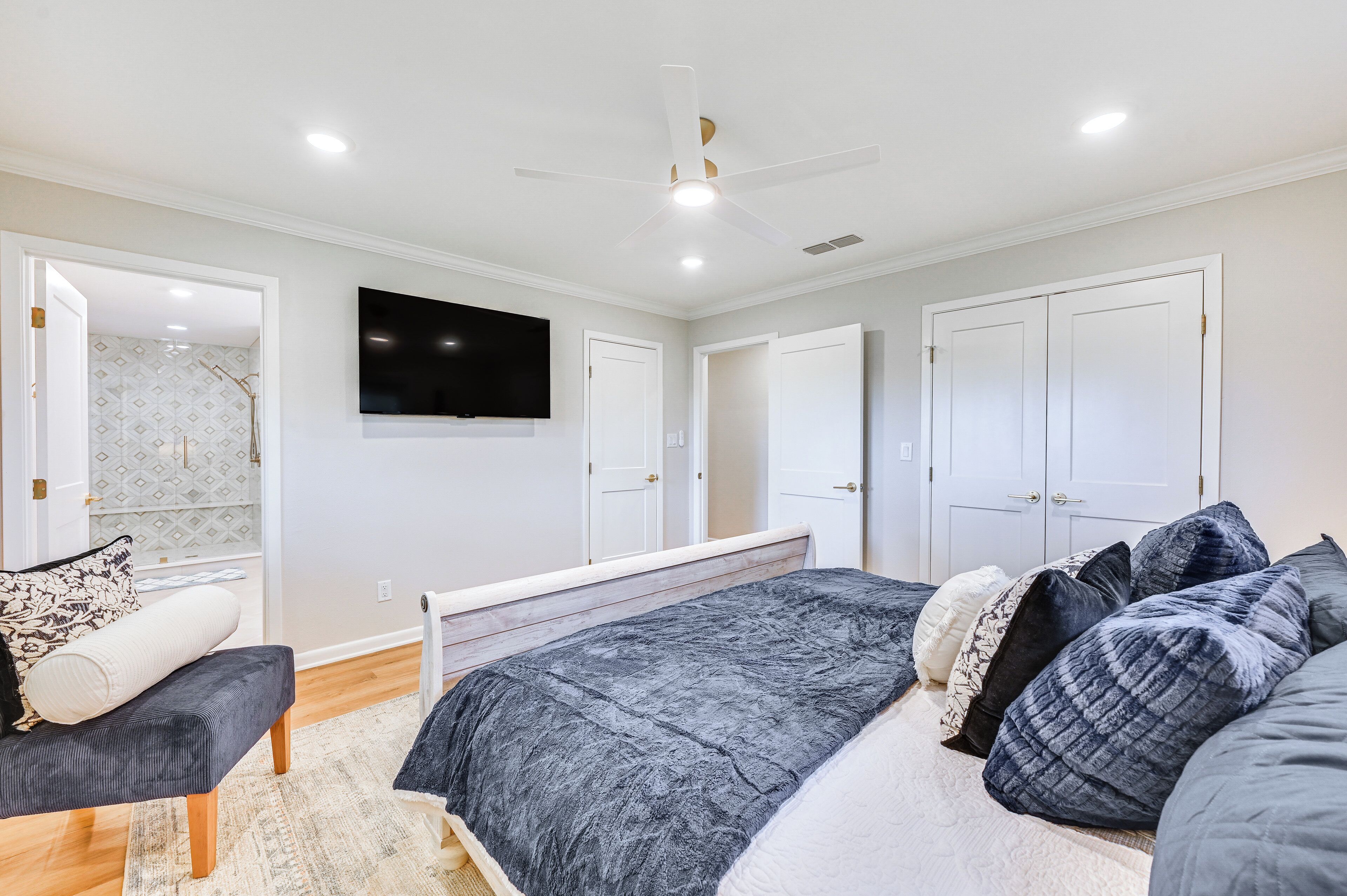 A bedroom with a bed, a bench, a TV, and a ceiling fan.