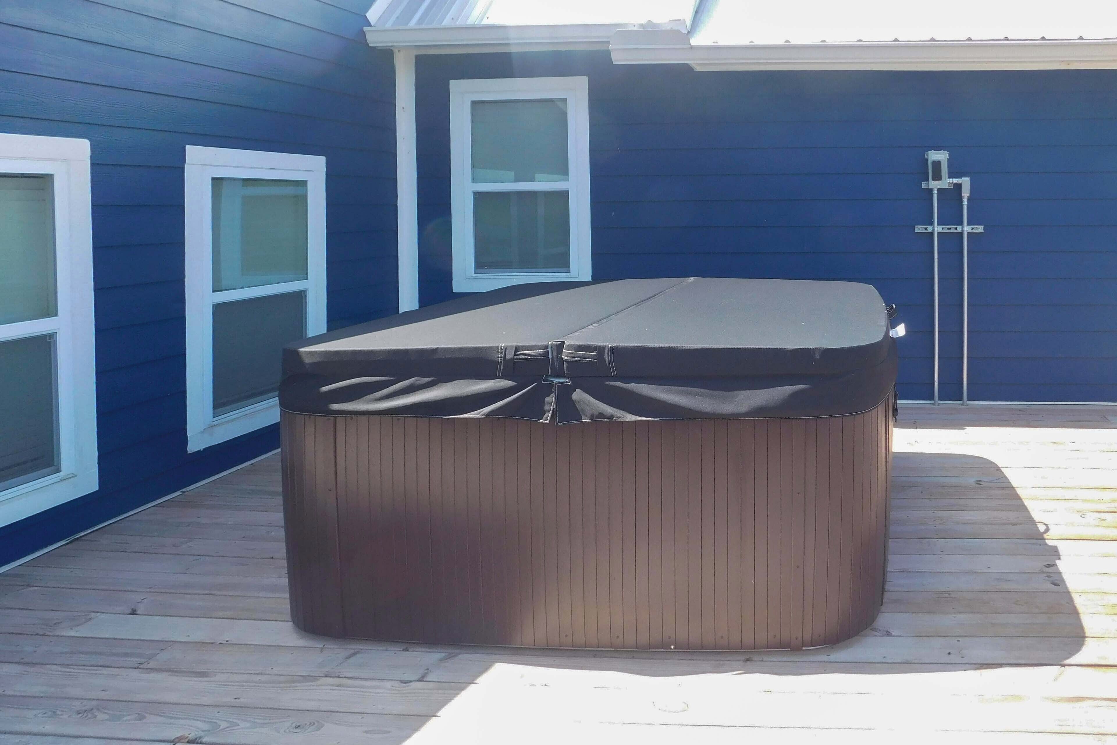 Een hottub op een houten terras, met een blauw huis op de achtergrond.