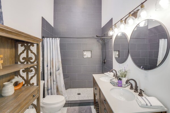 A modern bathroom with a shower, toilet, vanity with a mirror, and a sink. - Group Getaway: Lakefront Retreat in Fayetteville! (Fayetteville)