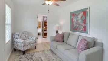 A living room with a ceiling fan, a patterned armchair, a grey sofa with patterned cushions, a rug, and a painting on the wall.
