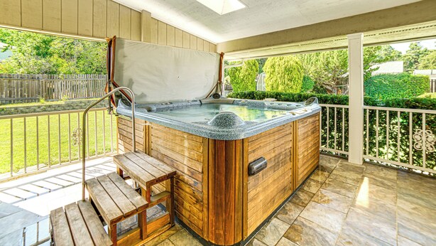 A wooden hot tub with a bench on a covered patio with a view of a garden. - Steps to Clear Lake: Hot Tub Haven in Norcal! (Lakeport)