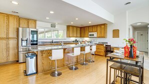 A modern kitchen with wooden cabinets, stainless steel appliances, a marble countertop, and a bar area with stools. - Steps to Clear Lake: Hot Tub Haven in Norcal! (Lakeport)