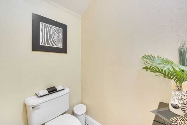 A bathroom with a white toilet, a small trash bin, and a framed zebra artwork on the wall.