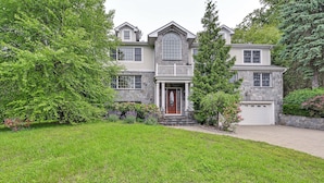 A two-story house with a stone facade, a front porch, and a garage. - Private Pool & Patio: Luxe Westchester Home! (Briarcliff Manor)